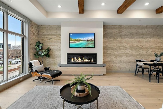 living room featuring wood finished floors, a glass covered fireplace, beamed ceiling, and brick wall