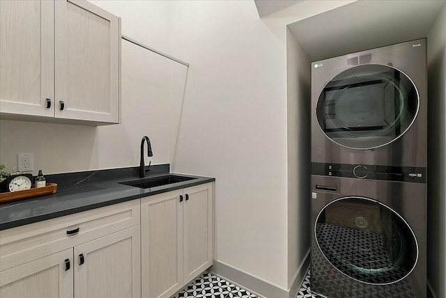laundry room featuring stacked washer and clothes dryer, cabinet space, a sink, and baseboards