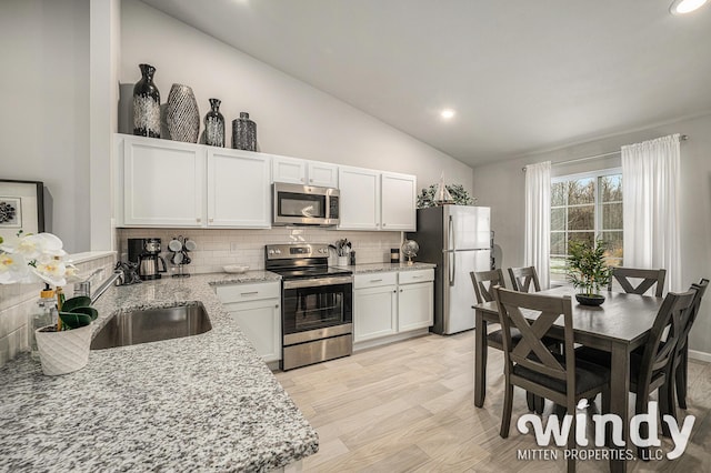 kitchen featuring a sink, white cabinets, vaulted ceiling, appliances with stainless steel finishes, and backsplash