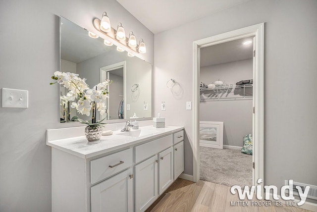 bathroom featuring a spacious closet, wood finished floors, vanity, and baseboards