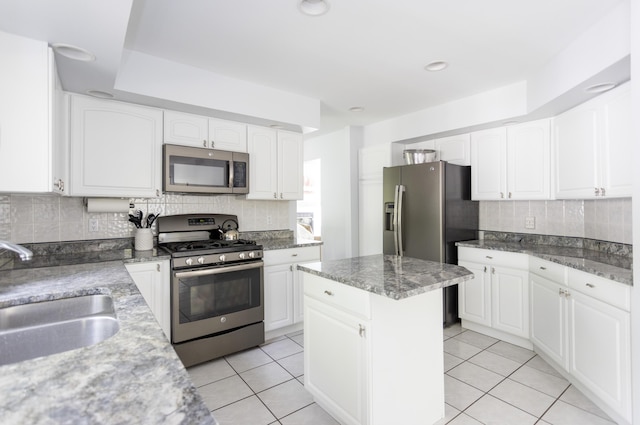 kitchen with light tile patterned floors, white cabinets, a sink, stainless steel appliances, and backsplash