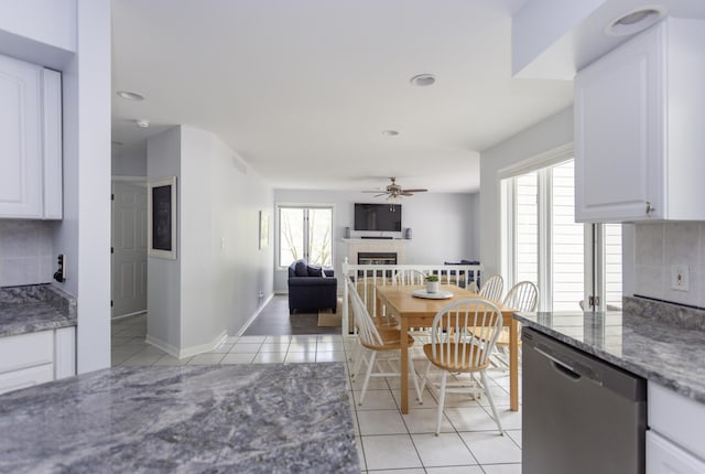 kitchen featuring light tile patterned floors, white cabinetry, stainless steel dishwasher, and a tile fireplace