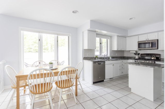 kitchen featuring appliances with stainless steel finishes, white cabinetry, backsplash, and dark stone countertops
