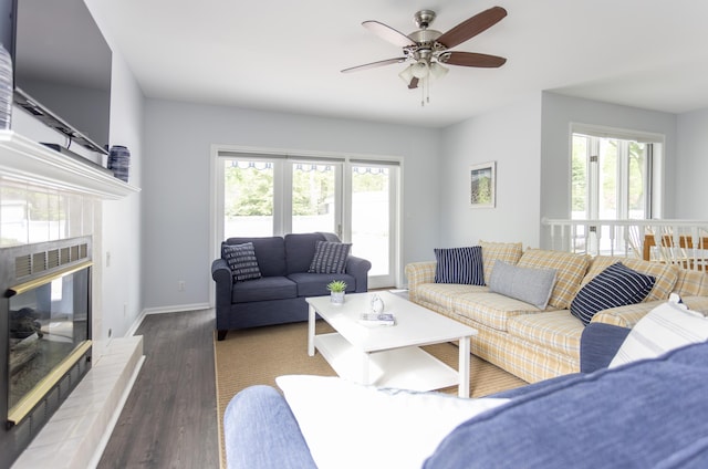 living area featuring a tile fireplace, a healthy amount of sunlight, baseboards, and wood finished floors