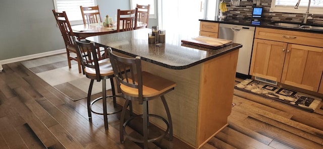 kitchen with dark wood-style floors, a breakfast bar, tasteful backsplash, stainless steel dishwasher, and a sink