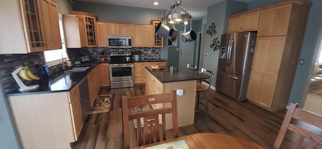 kitchen featuring dark wood-type flooring, a kitchen island, appliances with stainless steel finishes, backsplash, and dark countertops