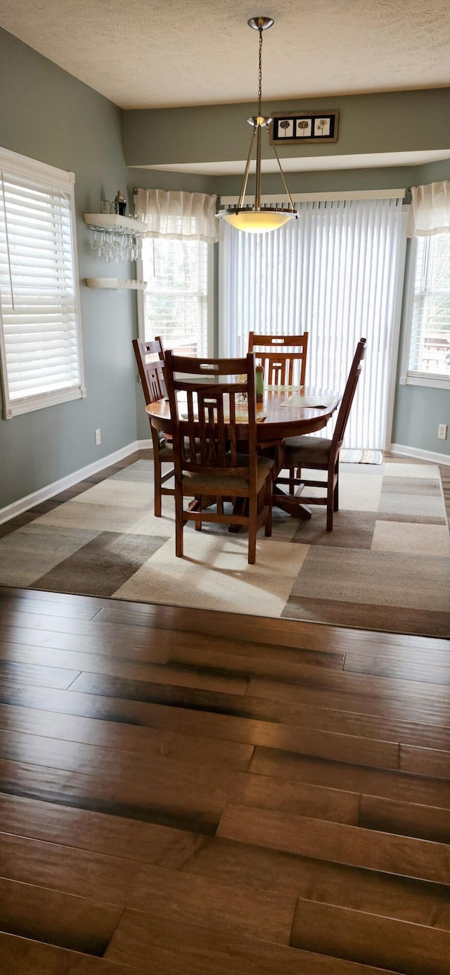 dining area with a textured ceiling, hardwood / wood-style floors, and baseboards