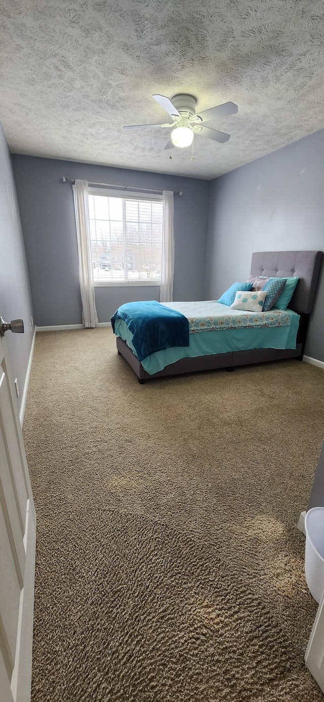 bedroom with carpet, a textured ceiling, baseboards, and a ceiling fan