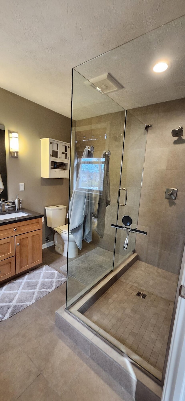 bathroom featuring toilet, a textured ceiling, a shower stall, vanity, and baseboards