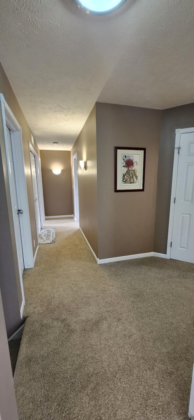 hall featuring a textured ceiling, carpet flooring, and baseboards