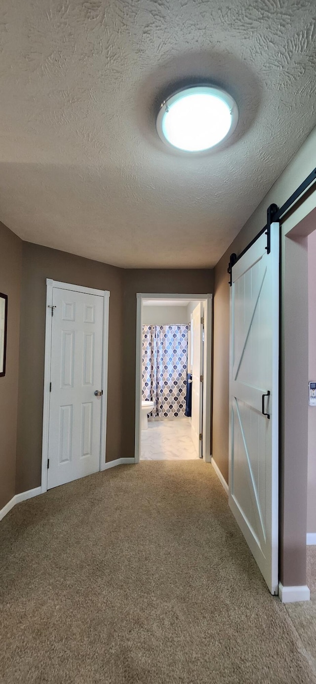 hallway featuring carpet, a textured ceiling, baseboards, and a barn door