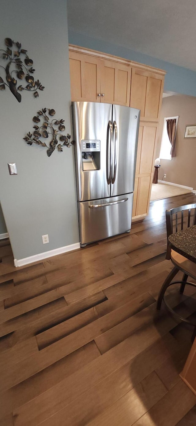 kitchen with dark wood-style flooring, stainless steel refrigerator with ice dispenser, baseboards, and light brown cabinetry