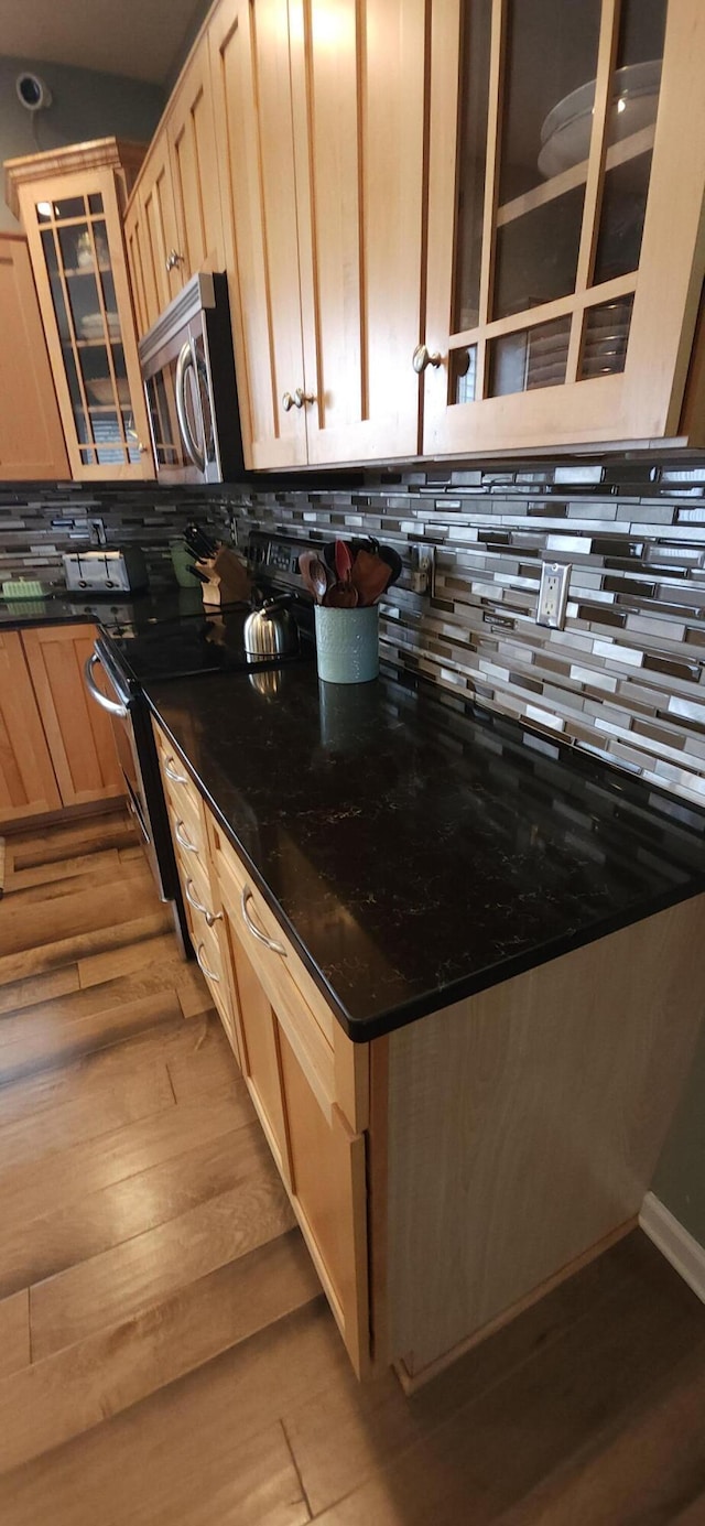 kitchen with appliances with stainless steel finishes, light wood-type flooring, light brown cabinetry, tasteful backsplash, and glass insert cabinets