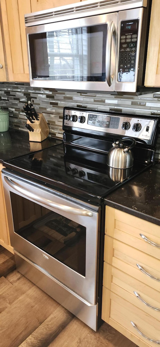 kitchen featuring dark countertops, decorative backsplash, appliances with stainless steel finishes, light brown cabinets, and wood finished floors