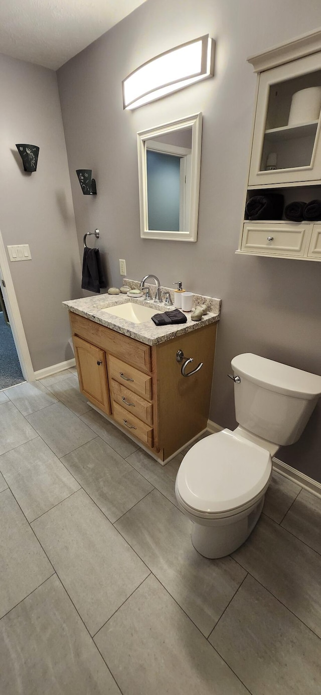 half bathroom with toilet, tile patterned flooring, baseboards, and vanity