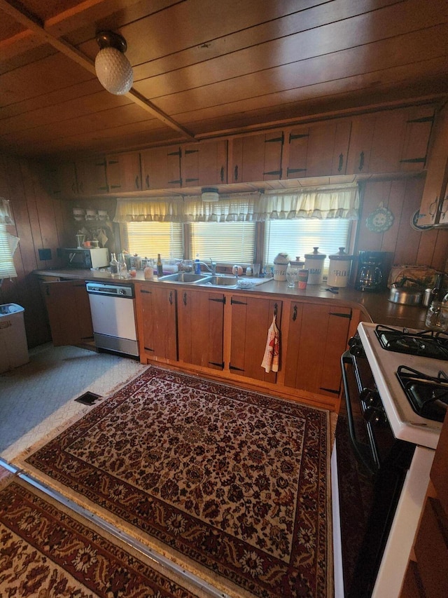 kitchen with gas range oven, stainless steel dishwasher, wood ceiling, a sink, and wood walls