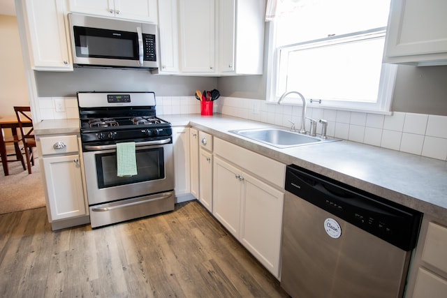 kitchen with stainless steel appliances, light countertops, backsplash, light wood-style floors, and a sink