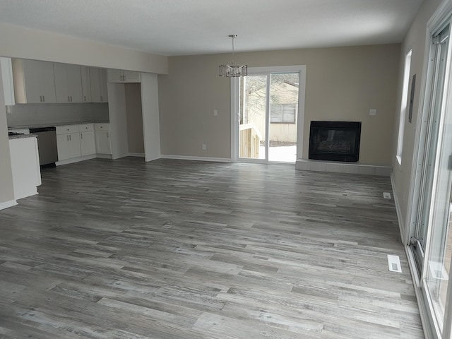 unfurnished living room featuring visible vents, baseboards, a tiled fireplace, wood finished floors, and a notable chandelier