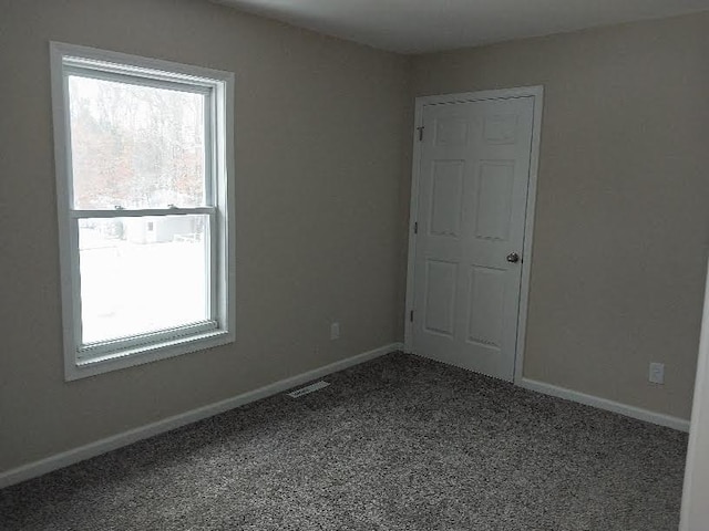 spare room featuring baseboards, visible vents, and dark colored carpet