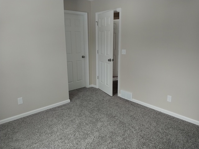 empty room featuring visible vents, dark carpet, and baseboards