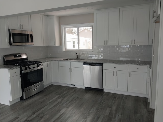 kitchen featuring light stone counters, dark wood finished floors, appliances with stainless steel finishes, white cabinetry, and a sink