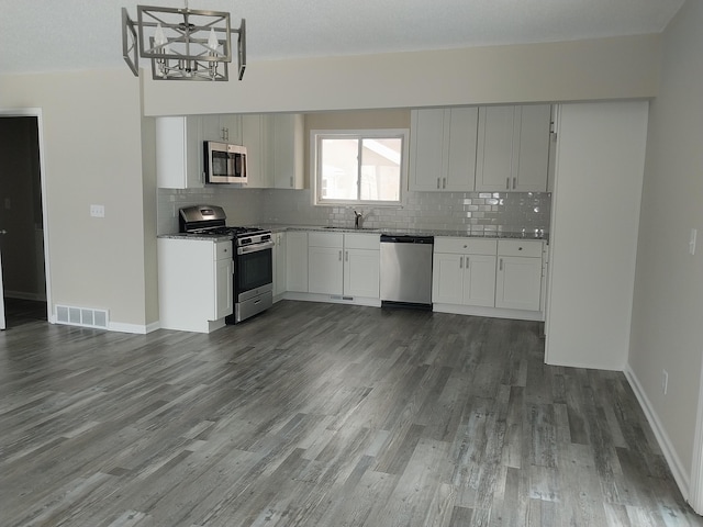 kitchen featuring stainless steel appliances, dark wood-style flooring, a sink, visible vents, and backsplash