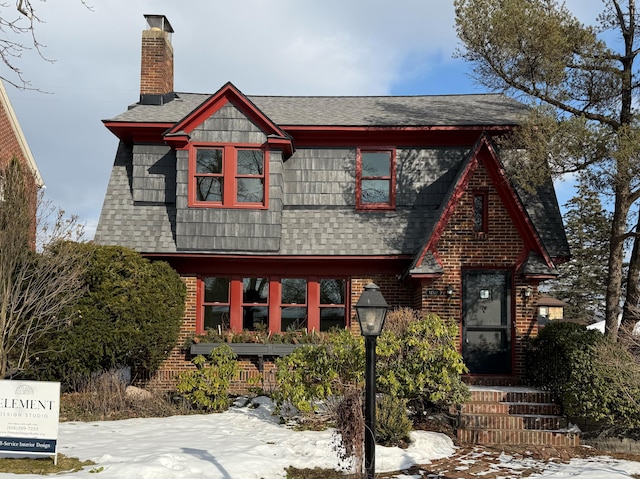 view of front facade with a shingled roof, brick siding, and a chimney