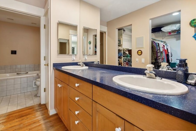 full bathroom with double vanity, a spacious closet, a sink, and a bath