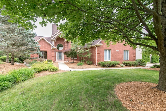 view of property hidden behind natural elements featuring a front lawn and brick siding