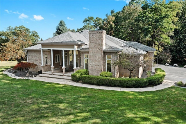 rear view of property with brick siding, a lawn, a chimney, and roof with shingles