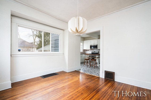 unfurnished dining area with visible vents, crown molding, baseboards, and wood finished floors