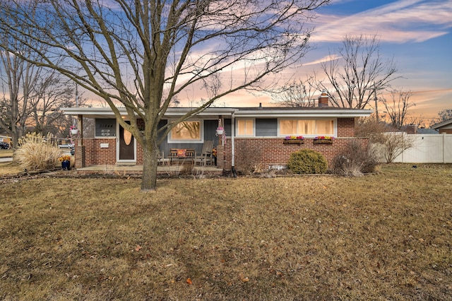 ranch-style house with brick siding, a chimney, a front lawn, and fence