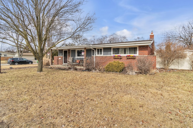 single story home featuring brick siding, covered porch, a chimney, and a front lawn