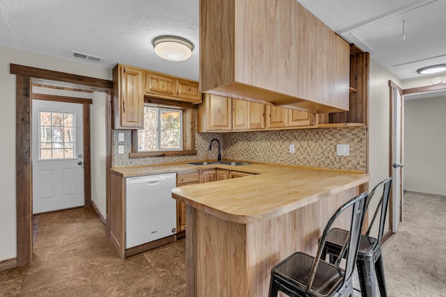 kitchen featuring visible vents, a kitchen breakfast bar, white dishwasher, light brown cabinetry, and a sink