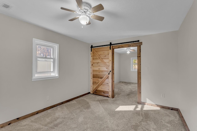 carpeted empty room featuring visible vents, ceiling fan, baseboards, and a barn door