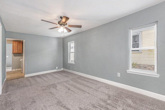 empty room with a ceiling fan, light carpet, and baseboards