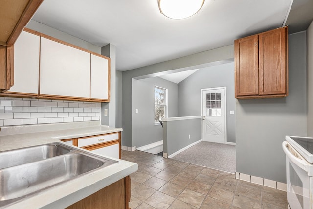 kitchen featuring baseboards, backsplash, vaulted ceiling, light countertops, and a sink