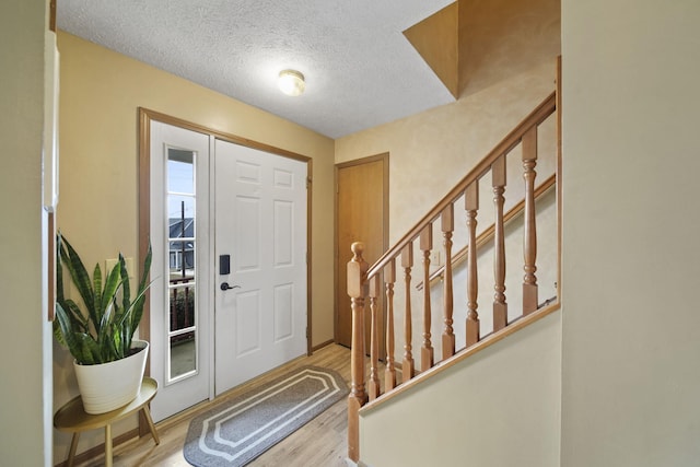 foyer entrance with a textured ceiling, stairway, and wood finished floors