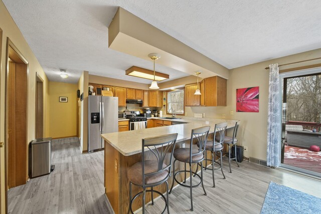 kitchen with stainless steel appliances, a wealth of natural light, light countertops, light wood-type flooring, and a peninsula