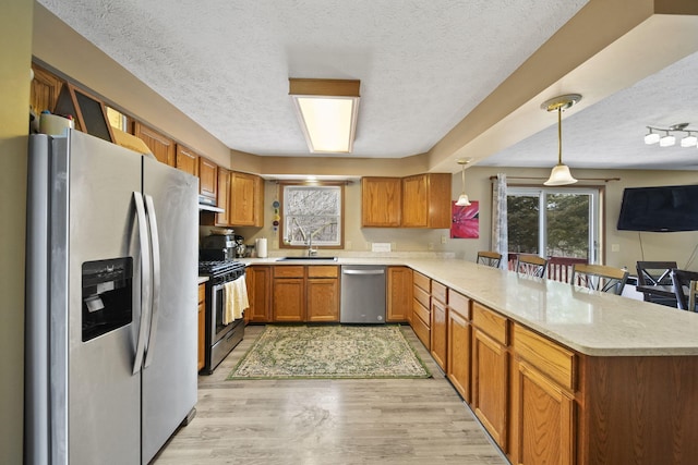 kitchen with brown cabinets, light wood finished floors, appliances with stainless steel finishes, a sink, and a peninsula