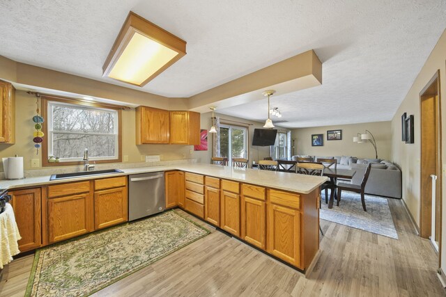 kitchen featuring a peninsula, a sink, light wood-style floors, open floor plan, and dishwasher