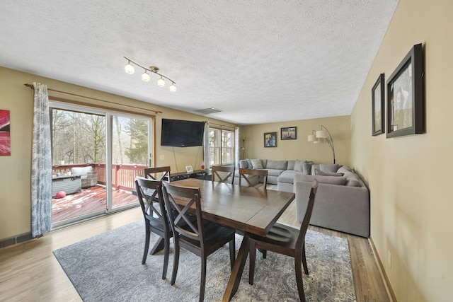 dining room featuring light wood-style floors, a textured ceiling, and baseboards