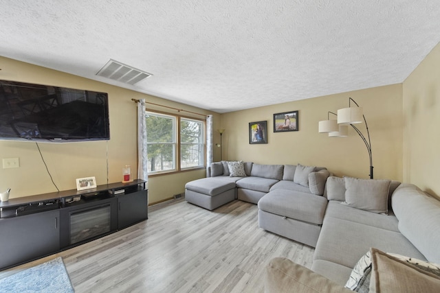 living room with a textured ceiling, visible vents, and light wood-style floors