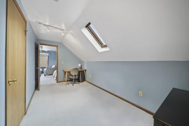 home office featuring track lighting, vaulted ceiling with skylight, light carpet, and baseboards