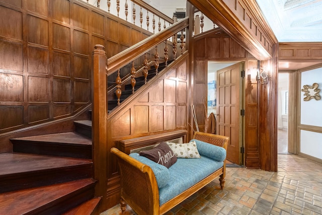 interior space featuring stairway, ornamental molding, brick floor, wood walls, and a decorative wall