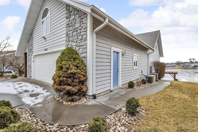 view of side of home with stone siding, an attached garage, and central air condition unit