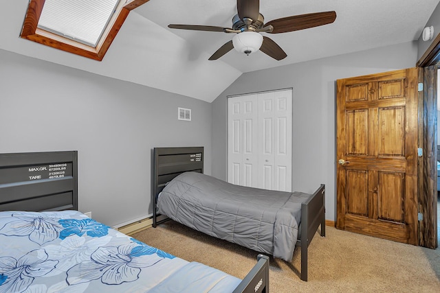 bedroom featuring ceiling fan, vaulted ceiling with skylight, light carpet, visible vents, and a closet