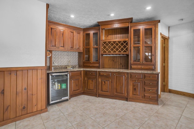 interior space with a textured ceiling, light tile patterned floors, wine cooler, a wainscoted wall, and wet bar