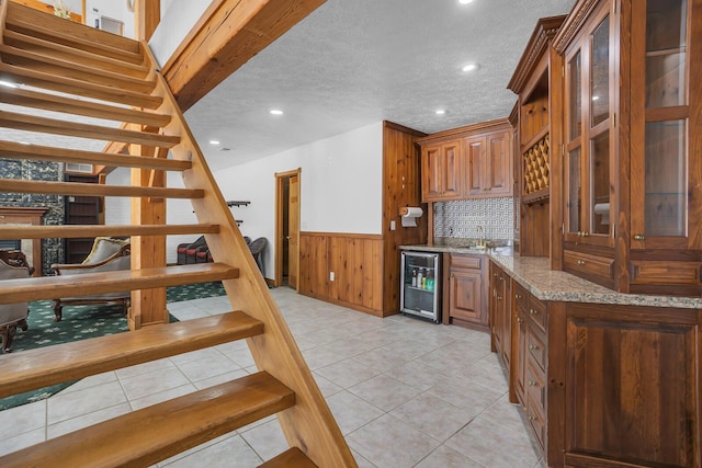 interior space featuring beverage cooler, brown cabinetry, wainscoting, and light stone countertops