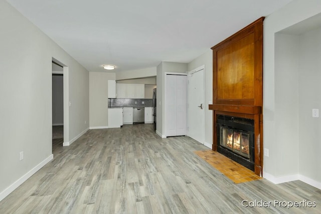 unfurnished living room featuring light wood-style floors, a large fireplace, and baseboards